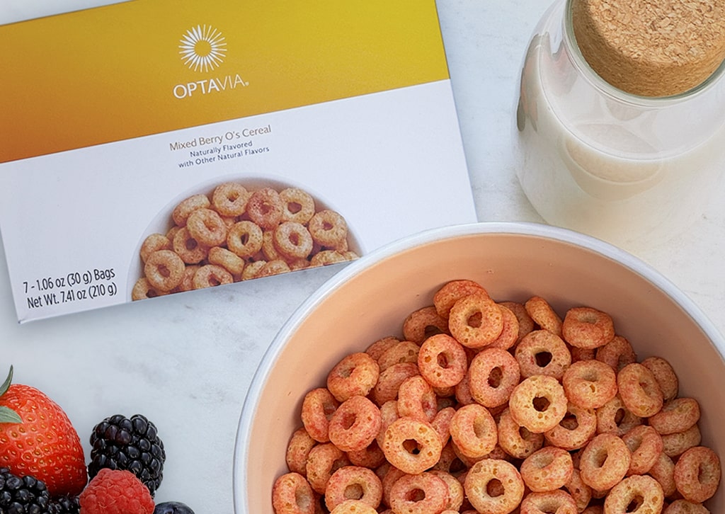 Optavia Mixed Berry O’s Cereal, packaging and bowl on a white countertop with fruit and milk.