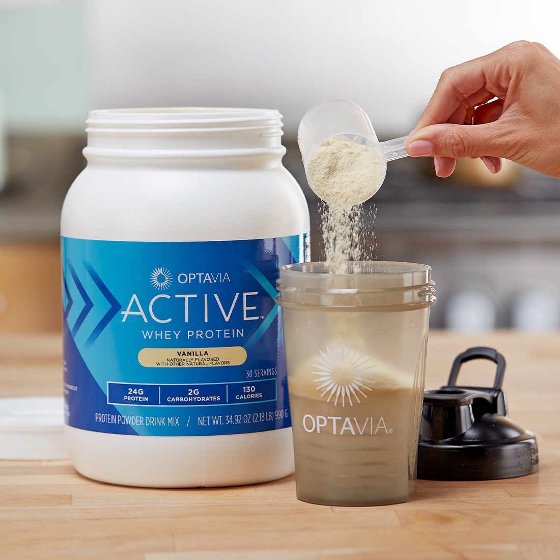 Hand adding a scoop of Optavia Active Whey Protein Blend, Vanilla to a blenderbottle.